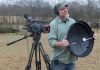 Shot of videographer holding a DIY parabolic mic dish, standing next to a camcorder on a tripod.