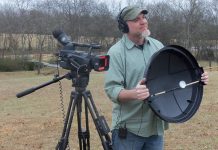 Shot of videographer holding a DIY parabolic mic dish, standing next to a camcorder on a tripod.